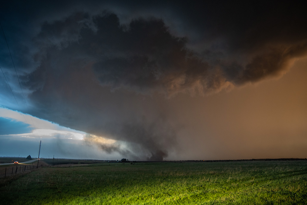 A truck is parked in the foreground, with a large storm system in the background.